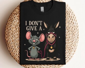 May include: Black t-shirt featuring a cartoon mouse and donkey with the text "I DON'T GIVE A." The mouse is gray with pink ears and a gold star. The donkey is black with a pink halter. The shirt is folded on a woven mat.