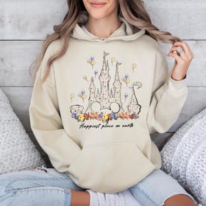 May include: A beige hoodie with a floral print of a castle and the text "Happiest place on earth".