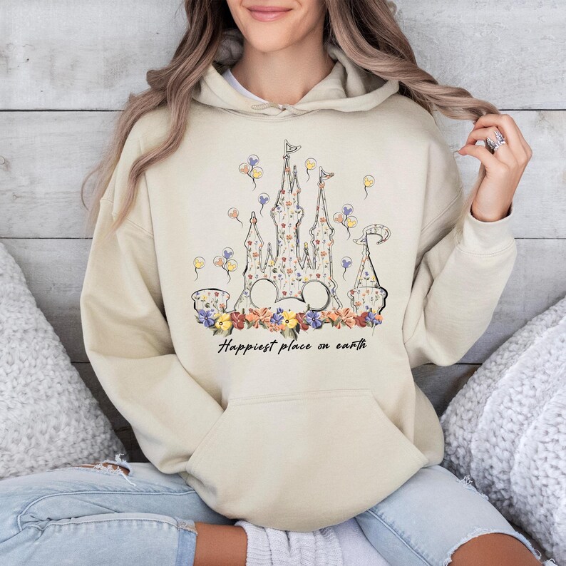 May include: A beige hoodie with a floral print of a castle and the text "Happiest place on earth".