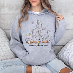 May include: A gray hoodie with a floral print of Cinderella's castle and the text "Happiest place on earth".