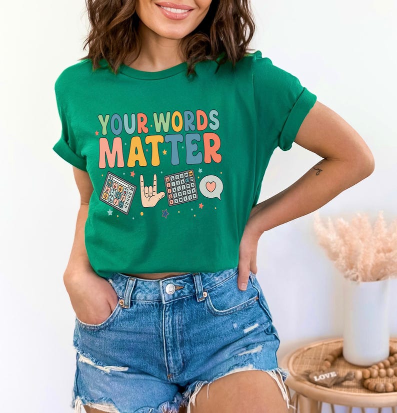 May include: A green t-shirt with the text "YOUR WORDS MATTER" in colorful letters. The shirt features graphic illustrations of a calculator, a hand signing "I love you" in sign language, and a speech bubble with a heart.