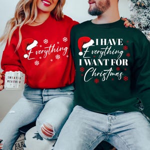 May include: Matching red and green Christmas sweaters. The red sweater says "Everything" with a Santa hat and snowflakes. The green sweater says "I have everything I want for Christmas" with a Santa hat and snowflakes.