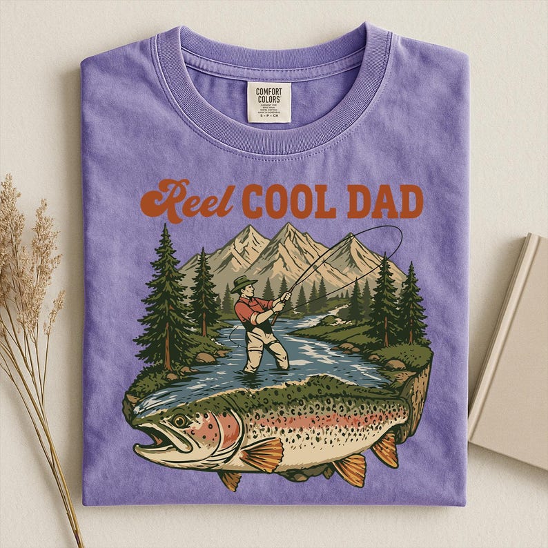 May include: A purple t-shirt with the words "Reel Cool Dad" in orange lettering. The graphic depicts a fisherman in a river with a large fish, mountains, and trees.