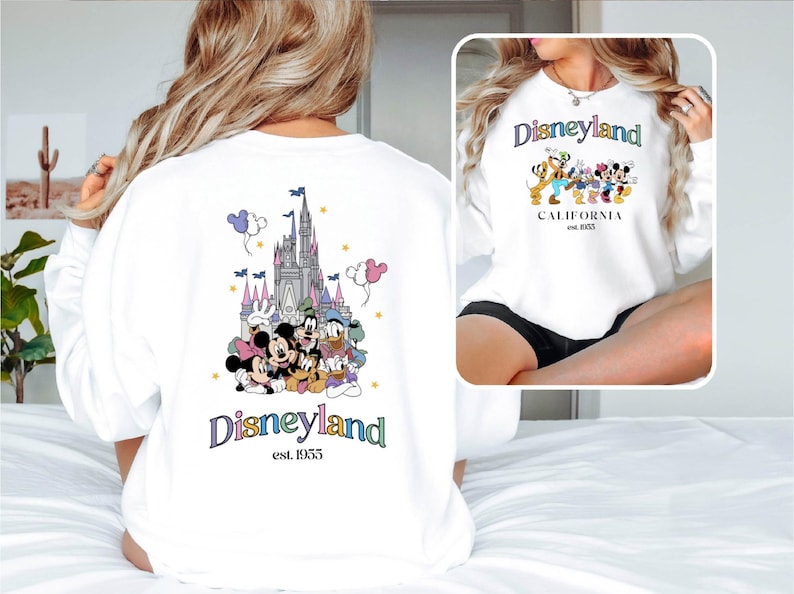Puede incluir: Sudadera blanca con un gr&aacute;fico de Disneyland colorido en la espalda. El gr&aacute;fico presenta a Mickey Mouse, Minnie Mouse, Donald Duck, Goofy y Pluto frente al Castillo de la Bella Durmiente. La parte delantera de la sudadera tiene un gr&aacute;fico de Disneyland m&aacute;s peque&ntilde;o con el texto "Disneyland est. 1955".