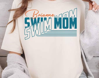 May include: A white t-shirt with the text "Brianne Swim Mom" in blue and orange lettering. The text is in a retro style with a layered effect.