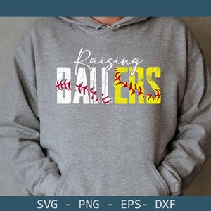 May include: A gray hoodie with the words "Raising Ballers" in white and yellow. The word "Ballers" is designed to look like a baseball with red stitching. The hoodie has a front pocket and a drawstring hood.