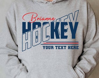 May include: A gray hoodie with a blue and white graphic that says "HOCKEY" with the name "Brianne" above it. The text "YOUR TEXT HERE" is below the graphic.