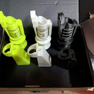 May include: Three 3D printed objects, one yellow, one white, and one black, each with a spring mechanism. The objects are in a box.