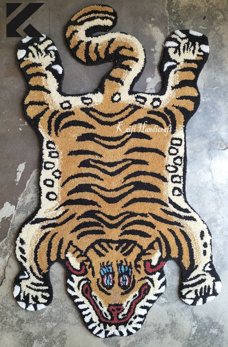 K&ouml;nnte beinhalten: Ein brauner und schwarzer Tigerteppich mit wei&szlig;em Umriss. Der Teppich besteht aus einem flauschigen Material und hat ein detailliertes Gesicht mit blauen Augen. Der Teppich ist in Form eines auf dem R&uuml;cken liegenden Tigers mit hochgestreckten Beinen geformt. Der Text "Kaifi Handicraft" ist in der Mitte des Teppichs sichtbar.