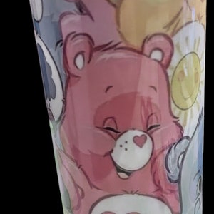 May include: A pink and white tumbler with a colorful Care Bears design. The tumbler features a rainbow, a yellow bear with a sun, and a pink bear with a heart.
