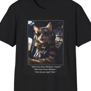 May include: A black t-shirt with a graphic of a cat wearing aviator sunglasses and a pilot's jacket. The cat is sitting in the cockpit of an airplane. The text on the t-shirt reads: "Mike Echo Oscar Whiskey! I repeat!" "Mike Echo Oscar Whiskey!" "How do you copy?! Over"