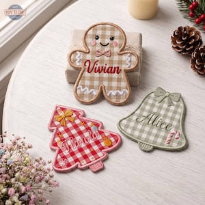May include: Three embroidered fabric ornaments featuring a gingerbread person with the name Vivian, a Christmas tree with the name Harold, and a bell with the name Alice. Each ornament displays a gingham pattern in tan, red, or sage green colors.