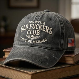 May include: A dark gray baseball cap with the text "100% Bitter Old Fuckers Club Lifetime Member" in white. The cap features a skull with wings and an American flag patch.