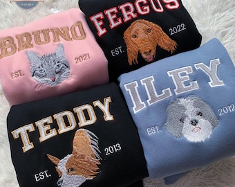May include: Four personalized sweatshirts with embroidered names and pet portraits. The sweatshirts are in pink, black, blue, and dark blue. The names are Bruno, Fergus, Teddy, and Iley. The pets are a cat, a dog, a dog, and a dog. The years are 2021, 2022, 2013, and 2012.