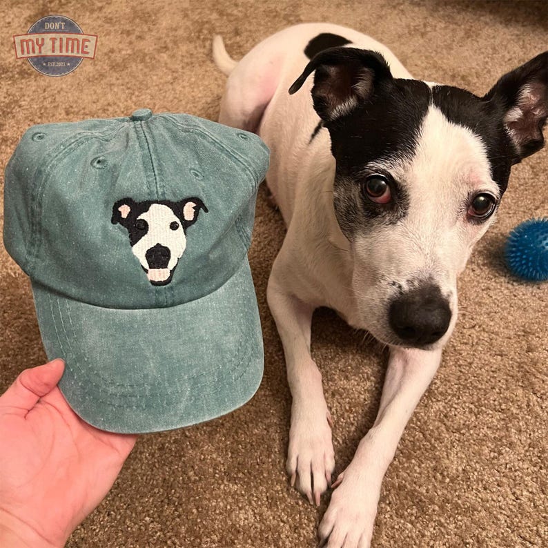 May include: A teal blue baseball cap with a white dog embroidered on the front. The dog has black ears, eyes, and nose. The cap has a white embroidered patch on the front that says "Don't My Time".