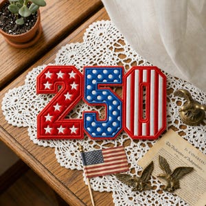 May include: A decorative number 250 sign featuring a red number 2 with white stars, a blue number 5 with white polka dots, and a red and white striped number 0. The numbers are outlined in red and have a stitched fabric appearance.