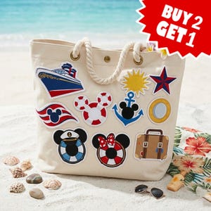 May include: A cream-coloured canvas tote bag with rope handles, decorated with various nautical and character-themed patches including a cruise ship, a sun, a star, a porthole, a suitcase, and Mickey Mouse icons. Text reads BUY 2 GET 1.