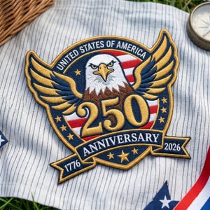 Peut inclure: Un écusson brodé représentant un pygargue à tête blanche aux ailes déployées sur un motif de drapeau rouge, blanc et bleu. Le texte indique UNITED STATES OF AMERICA, 250 ANNIVERSARY, 1776 et 2026. L'écusson est bleu marine, doré, rouge et blanc.