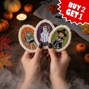 Può includere: Tre toppe ricamate di forma ovale raffiguranti personaggi dei cartoni animati in costumi di Halloween. La toppa a sinistra mostra un ranger spaziale, quella centrale un fantasma e quella a destra una cowgirl con un cappello da strega.