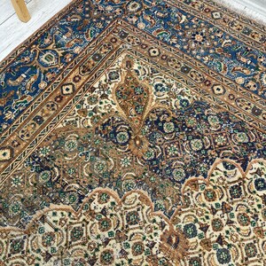 May include: A vintage rug with a cream background and intricate patterns in shades of blue, brown, and green. The rug has a faded, distressed look, adding to its antique charm.