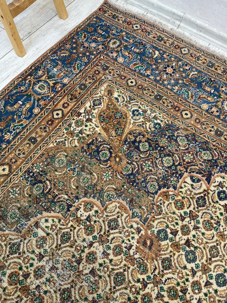 May include: A vintage rug with a cream background and intricate patterns in shades of blue, brown, and green. The rug has a faded, distressed look, adding to its antique charm.