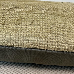 May include: A rectangular throw pillow featuring a top section made of a thick, beige, textured woven fabric with a prominent looped pile. The bottom section consists of a smooth, dark brown fabric panel with a fine, uniform ribbed texture.