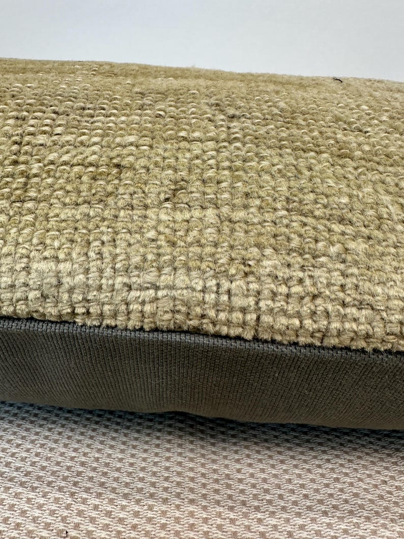 May include: A rectangular throw pillow featuring a top section made of a thick, beige, textured woven fabric with a prominent looped pile. The bottom section consists of a smooth, dark brown fabric panel with a fine, uniform ribbed texture.