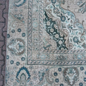 Puede incluir: Una alfombra vintage con un fondo crema descolorido y un patr&oacute;n floral azul y verde. La alfombra tiene un borde deshilachado y un aspecto desgastado.