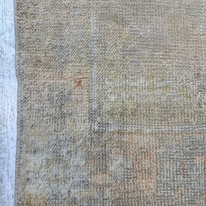 May include: A close-up of a beige rug with a woven texture. The rug has a fringe border and is made of natural fibers.