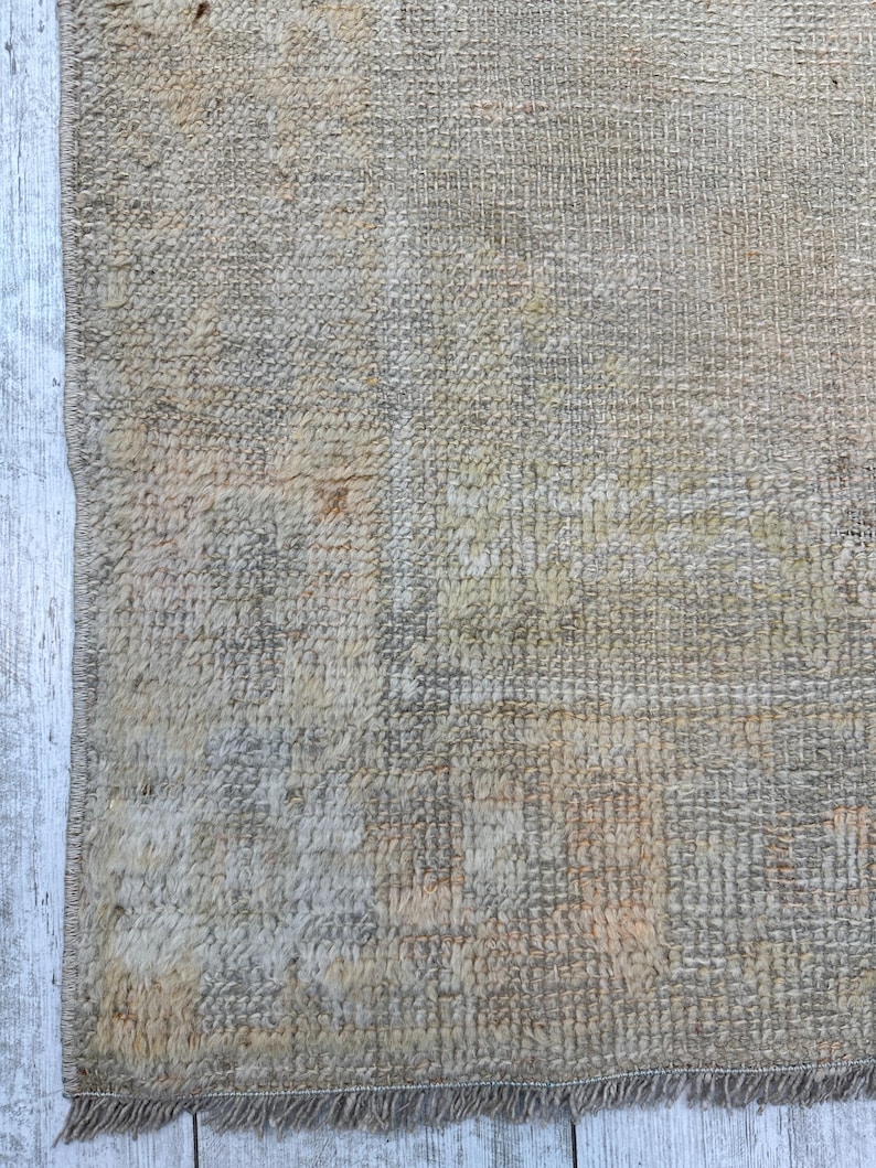 May include: A close-up of a beige rug with a woven texture. The rug has a fringe border and is made of natural fibers.