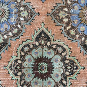 May include: Close-up of a vintage rug with a detailed floral pattern in shades of brown, blue, green, and pink.