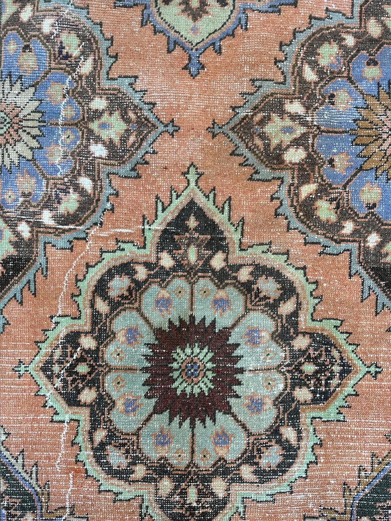 May include: Close-up of a vintage rug with a detailed floral pattern in shades of brown, blue, green, and pink.