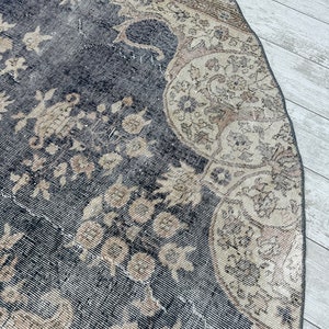 K&ouml;nnte beinhalten: Ein runder, vintage Teppich mit schwarzem Hintergrund und einem beigefarbenen Blumenmuster. Der Teppich hat einen abgenutzten Look und ist aus einem weichen, gewebten Material gefertigt.