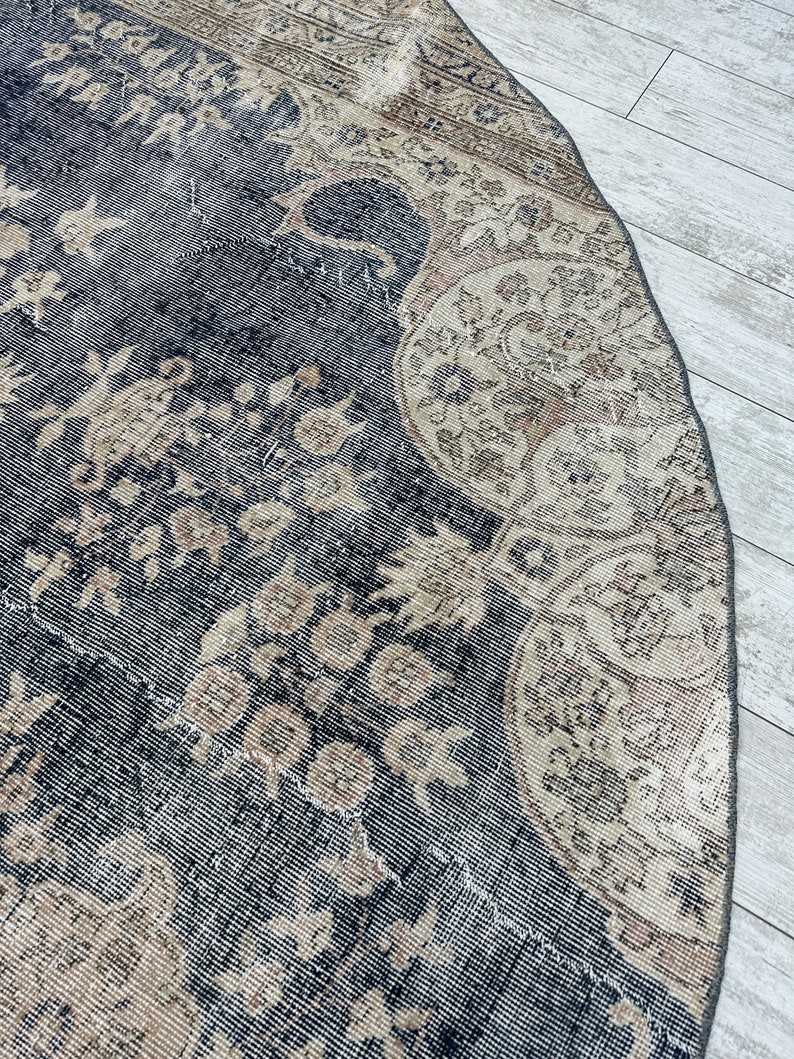 K&ouml;nnte beinhalten: Ein runder, vintage Teppich mit schwarzem Hintergrund und einem beigefarbenen Blumenmuster. Der Teppich hat einen abgenutzten Look und ist aus einem weichen, gewebten Material gefertigt.