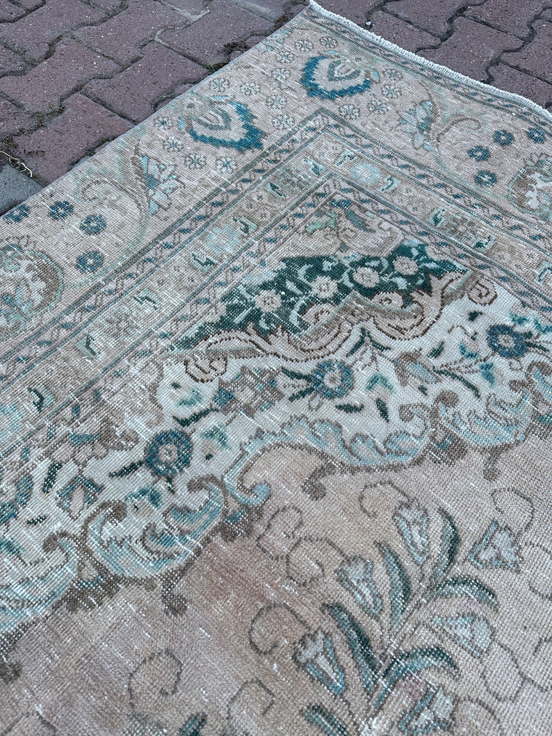 Puede incluir: Una alfombra vintage con un patr&oacute;n floral descolorido en tonos beige, azul y verde. La alfombra tiene un aspecto desgastado y est&aacute; hecha de un material suave y tejido.