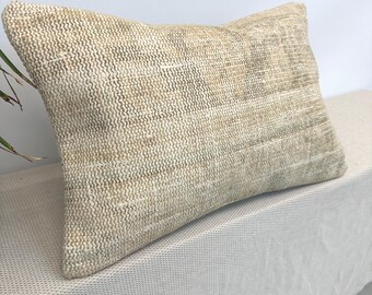 May include: A rectangular beige pillow with a textured, woven appearance. The pillow has a neutral color palette, with variations of beige and tan. The fabric appears to have a subtle, ribbed pattern, adding visual interest. The pillow is likely for home decor.