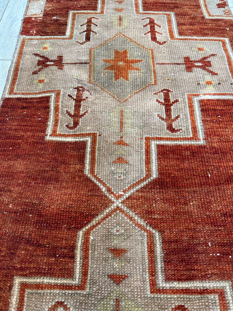 May include: A vintage runner rug with a geometric pattern in shades of brown, beige, and white. The rug has a distressed look and is made of a woven material.