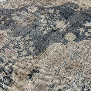 K&ouml;nnte beinhalten: Ein Vintage-Teppich mit einem verblassten, komplizierten Muster in Beige-, Braun- und Schwarzt&ouml;nen. Der Teppich hat einen abgenutzten, verwitterten Look, der ihm ein rustikales und antikes Aussehen verleiht.