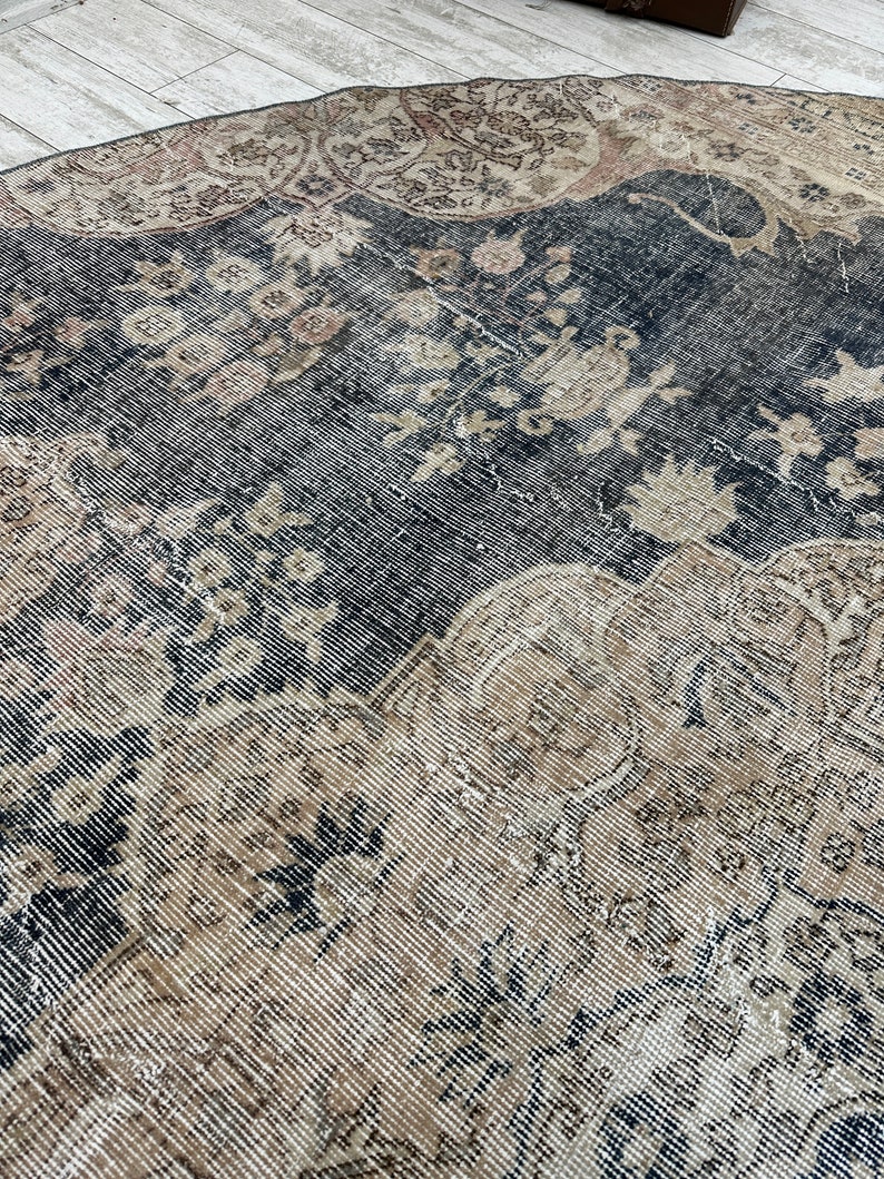 K&ouml;nnte beinhalten: Ein Vintage-Teppich mit einem verblassten, komplizierten Muster in Beige-, Braun- und Schwarzt&ouml;nen. Der Teppich hat einen abgenutzten, verwitterten Look, der ihm ein rustikales und antikes Aussehen verleiht.