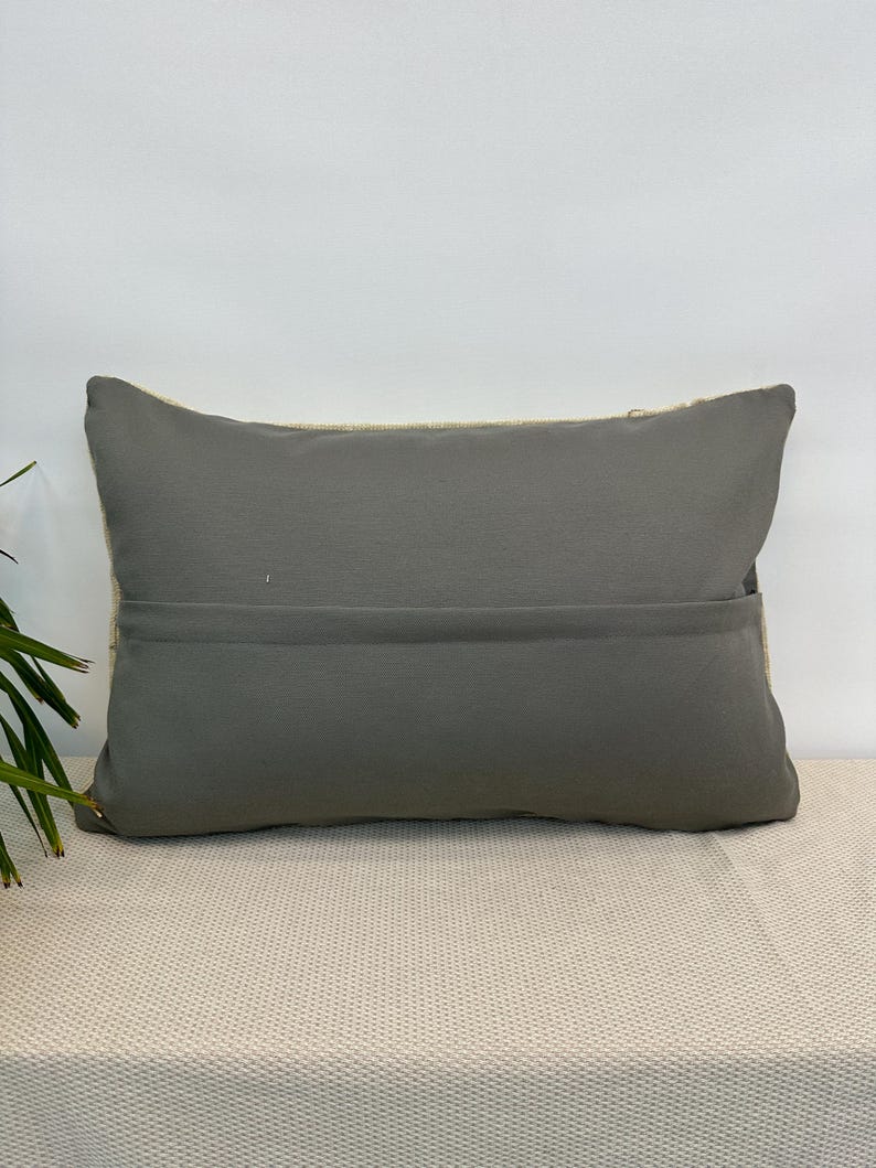 May include: A rectangular throw cushion featuring a solid dark grey fabric front with a horizontal seam across the middle. The cushion has a visible light-coloured, textured woven fabric border along the top and sides, creating a distinct contrast.