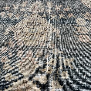 K&ouml;nnte beinhalten: Nahaufnahme eines schwarzen und beigefarbenen Teppichs mit gewebter Struktur. Der Teppich hat einen abgenutzten Look mit verblassten Bereichen und einem dezenten Blumendesign.