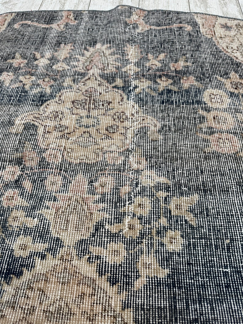 K&ouml;nnte beinhalten: Nahaufnahme eines schwarzen und beigefarbenen Teppichs mit gewebter Struktur. Der Teppich hat einen abgenutzten Look mit verblassten Bereichen und einem dezenten Blumendesign.
