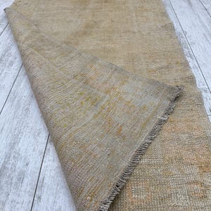 May include: A beige and brown woven rug with a fringed edge. The rug is folded in half and the texture of the weave is visible.