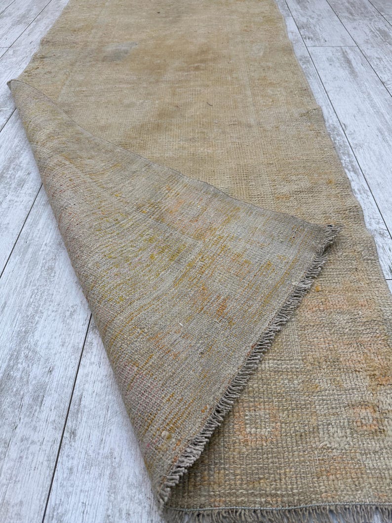 May include: A beige and brown woven rug with a fringed edge. The rug is folded in half and the texture of the weave is visible.
