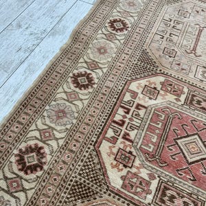 May include: A vintage Turkish rug with a beige background and intricate geometric patterns in shades of brown, pink, and red.