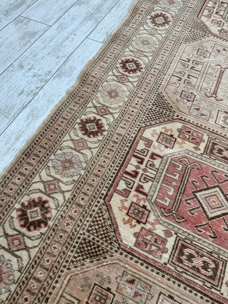 May include: A vintage Turkish rug with a beige background and intricate geometric patterns in shades of brown, pink, and red.