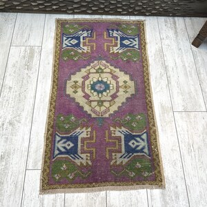 May include: A rectangular, hand-woven rug with a central medallion design. The rug features a vibrant magenta field with geometric patterns in blue, green, and beige. The border is a contrasting gold color. The rug is approximately 24 x 36 inches.