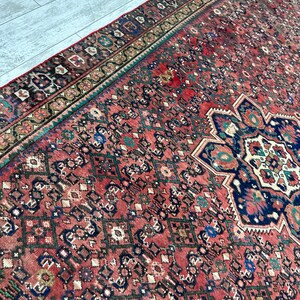 May include: A vintage Persian rug with a red background and intricate geometric patterns in shades of blue, green, and brown. The rug has a faded, worn look, adding to its antique charm.
