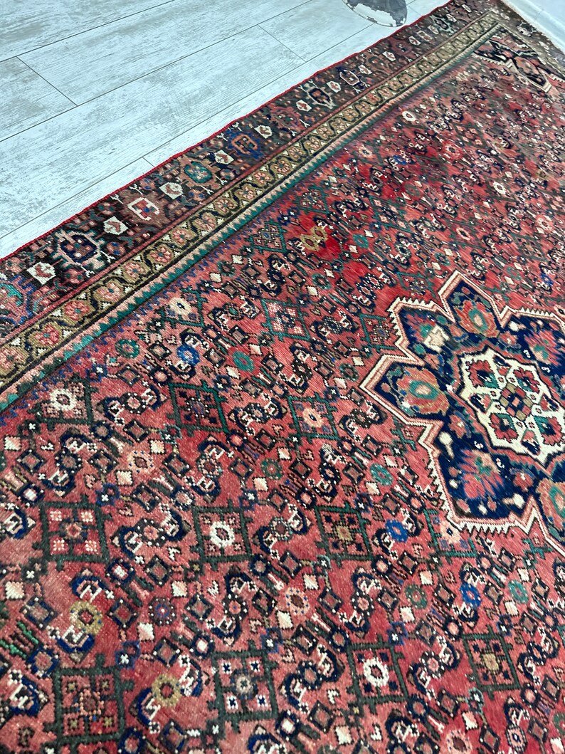 May include: A vintage Persian rug with a red background and intricate geometric patterns in shades of blue, green, and brown. The rug has a faded, worn look, adding to its antique charm.