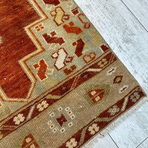 May include: A vintage rug with a brown, beige, and white geometric pattern. The rug has a fringe border and is made of wool.